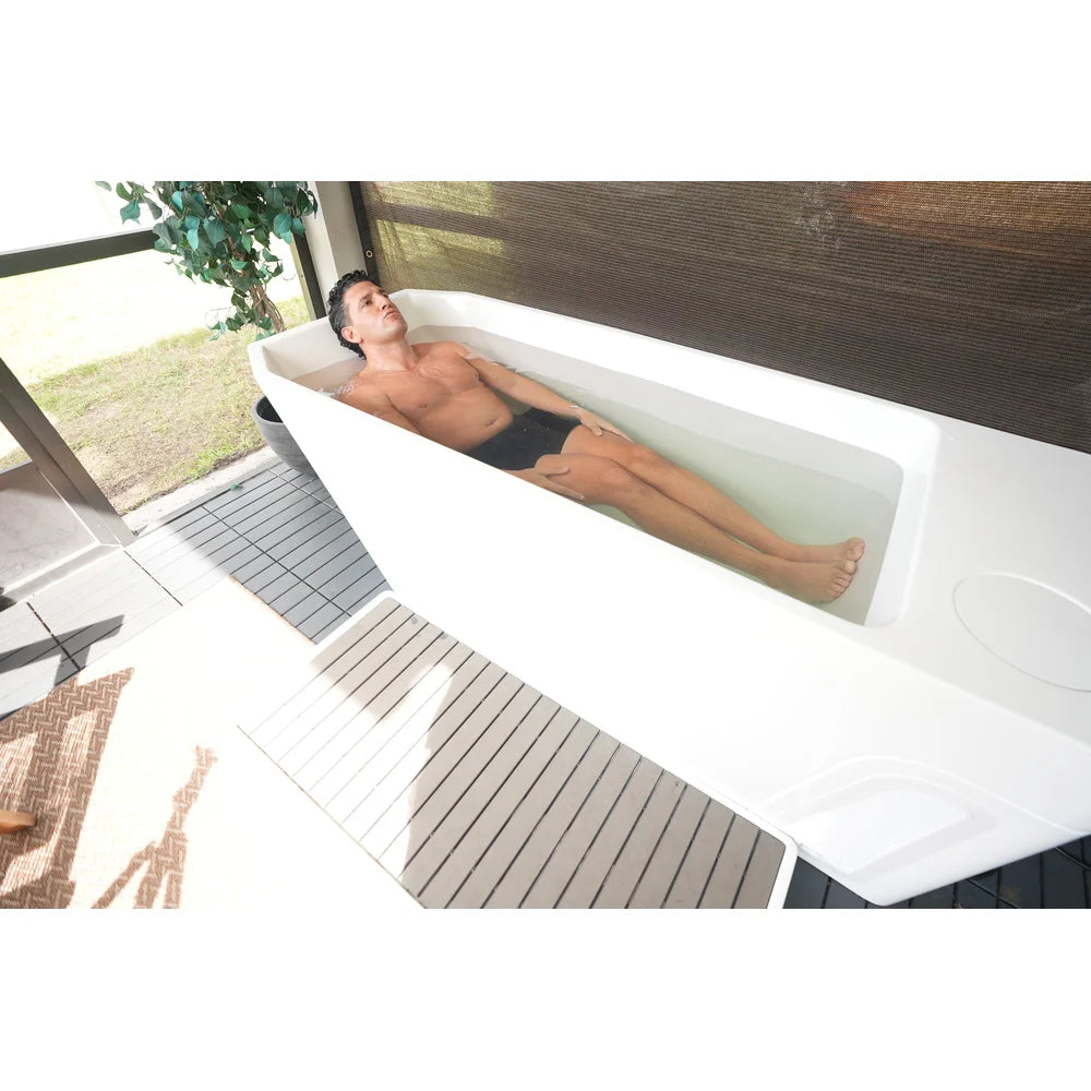 Man stretched out with legs extended in the AMBOHR All-in Ice Bath Machine tub on a screened porch