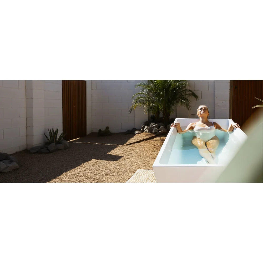 Wide courtyard banner of a woman reclining in the AMBOHR All-in Ice Bath Tubs unit beside a palm tree