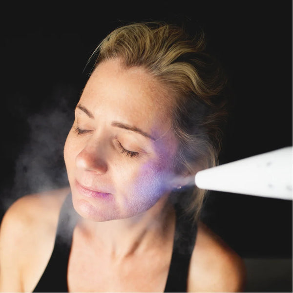 Cold plume from the America Cryo SubZero cryotherapy unit directed at a woman's cheek during a cryo facial