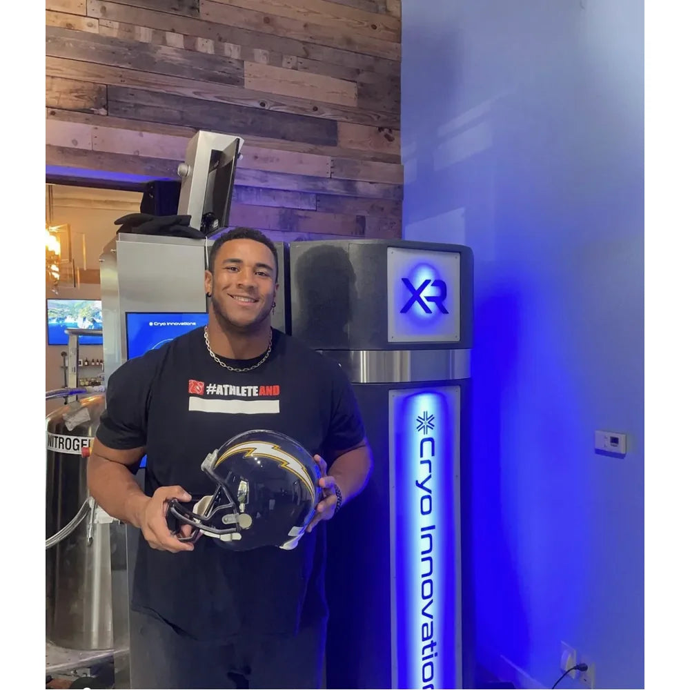 Football player with helmet standing next to blue-lit Cryo Innovations XR Cryotherapy Chambers on site