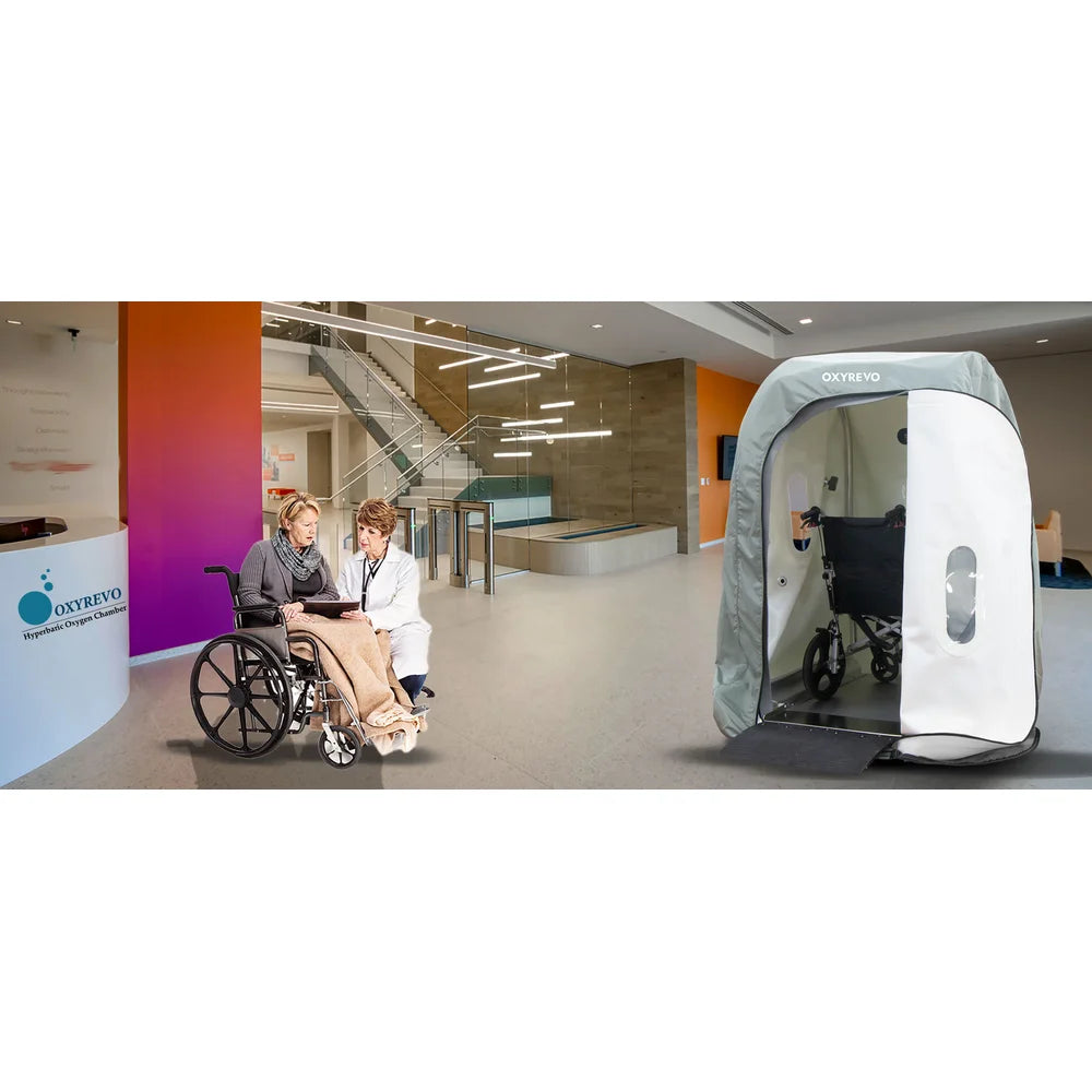 Nurse assisting a seated patient beside the open Oxyrevo Heal 40 Wheelchair Hyperbaric Chamber in a clinic lobby