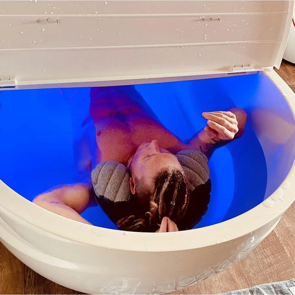 Man floating on a neck pillow inside the Dreampod Home Float Pro Float Tank under deep blue interior LED lighting