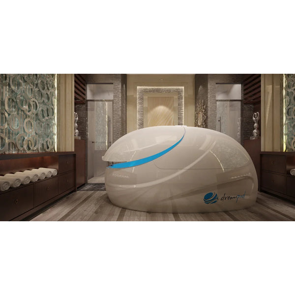Glossy white Dreampod V2 Isolation Tank with blue door light in a wood-floored spa room with rolled towels