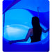 Woman stepping into an open Dreampod V2 Isolation Tank bathed in deep blue light above shallow salt water