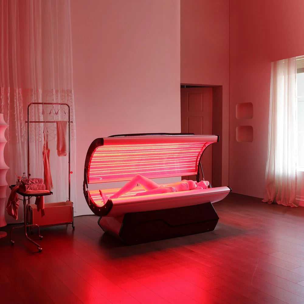 Person lying inside the open Galaxy Zero Capsule LED Light Therapy Bed during a full red light session in a treatment room