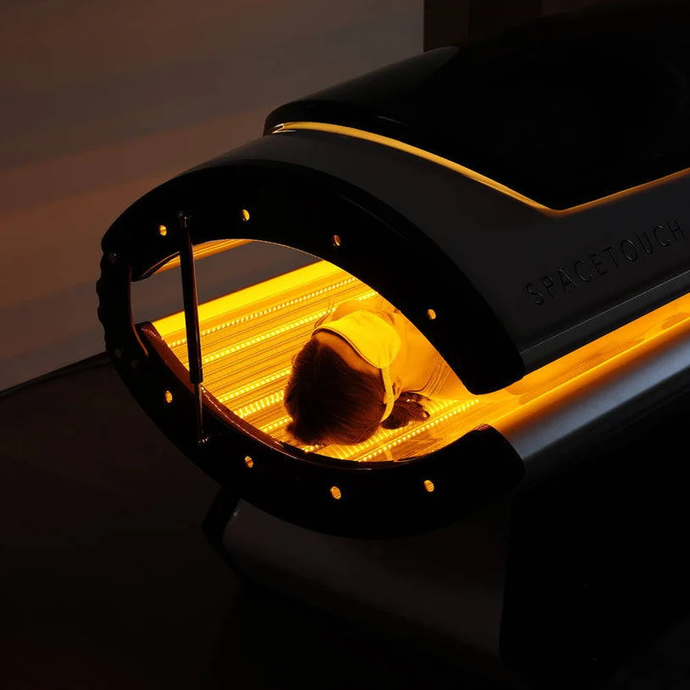 Golden yellow LED strips lighting the interior of the Spacetouch Capsule around a reclining woman wearing eye shields