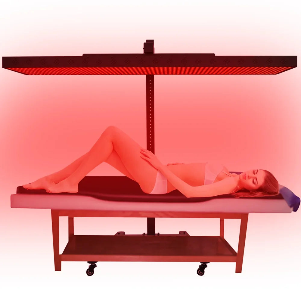Illuminated panel held over a massage table by the JKG Horizontal Rolling Stand for Red Light Therapy Panels in a red-toned studio