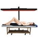 Full-body lying-down session under a lit panel supported by the JKG Rolling Stand for Red Light Therapy Panels above a table