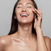Laughing model with glowing skin touching her cheek, illustrating results from the Galaxy Zero Atlas Full Body LED Therapy unit