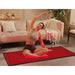 Woman stretching cross-legged on the lit pad beside a sofa, using Kore KoreKapsule Red Light Therapy Devices at home
