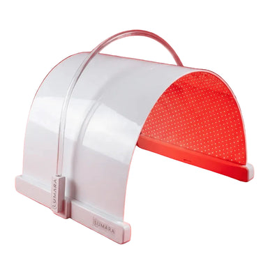 Curved white Lumara Illuminate Red Light Therapy Panel glowing on a red studio backdrop with clear carry handle