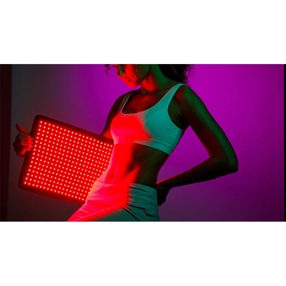 Woman in white activewear holding the glowing Lumara Pad Red Light Therapy Device at her hip under magenta lighting