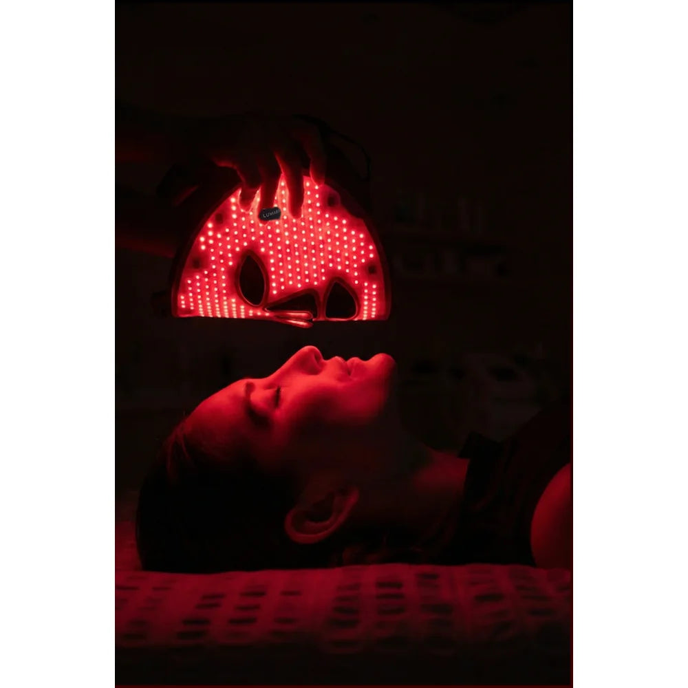 Hand lowering the glowing Lumara VISO over a client resting on a treatment bed in a darkened room