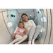 Smiling woman and young girl wearing nasal cannulas inside the Oxyrevo Forward90 Sitting Hyperbaric Chamber, teal cushions and lit windows behind them