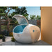 Egg-shaped Dreampod Home Float Plus Flotation Tank with lid open beside a zen rock garden