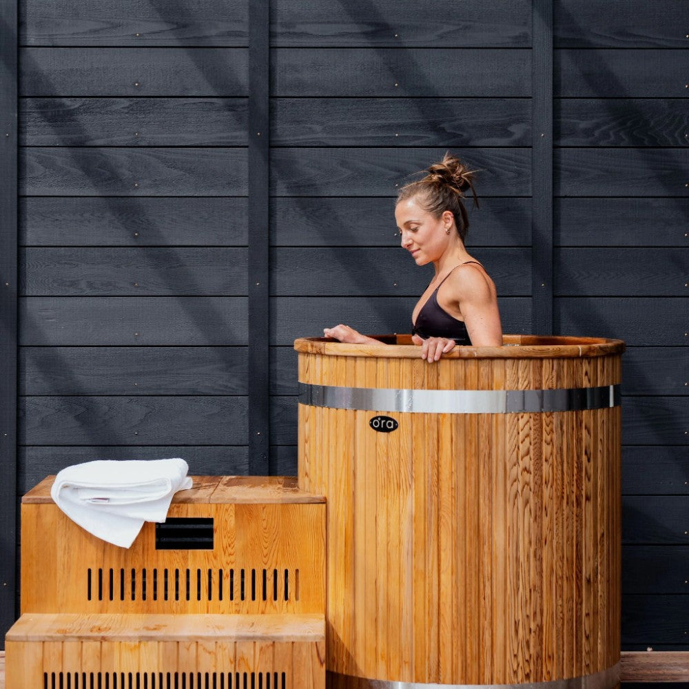 Woman cold plunging in the Ora Ice Bath red cedar barrel tub beside the cedar step chiller enclosure