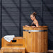 Woman cold plunging in the Ora Ice Bath red cedar barrel tub beside the cedar step chiller enclosure