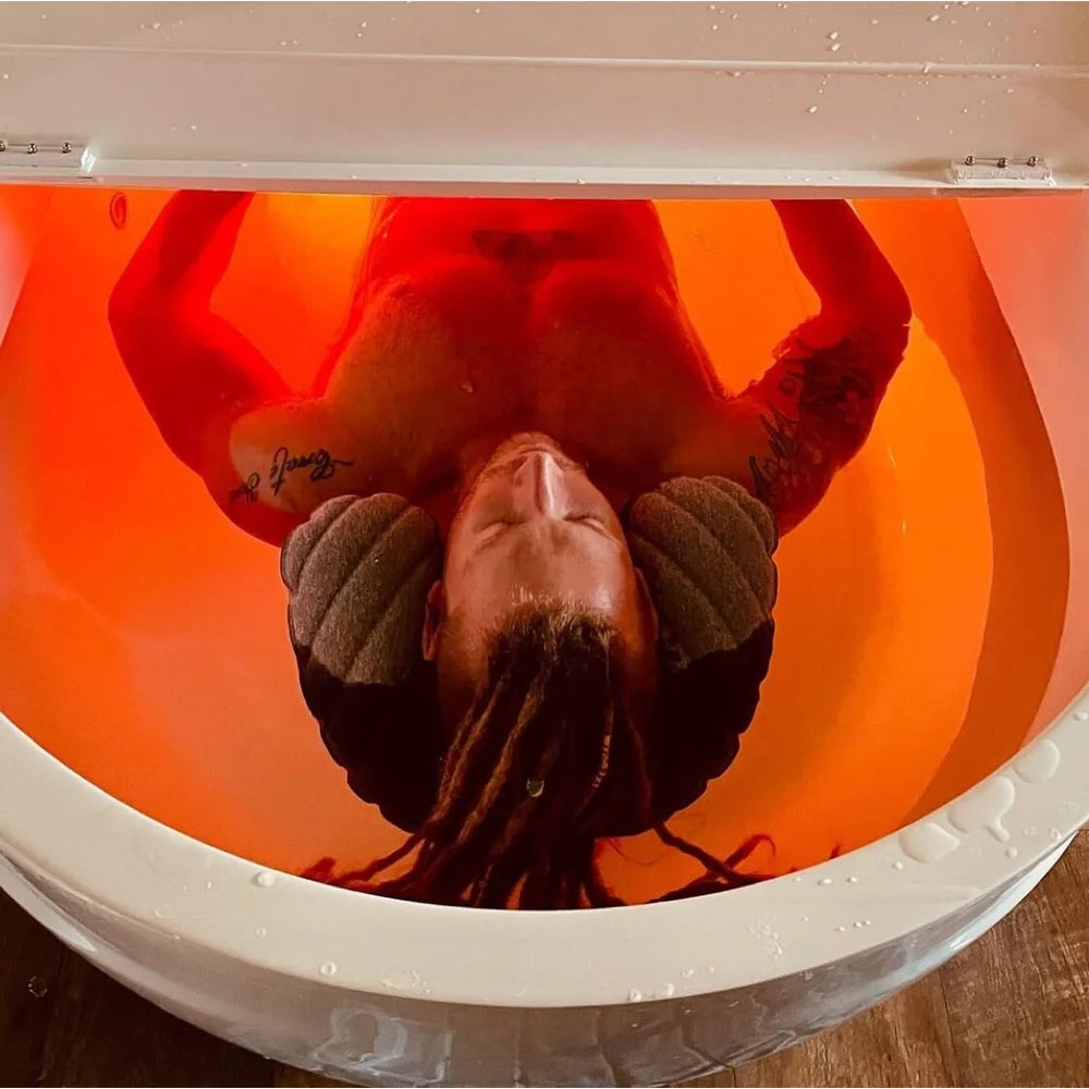 Person floating under orange LED lighting inside the Dreampod Home Float Plus Flotation Tank interior