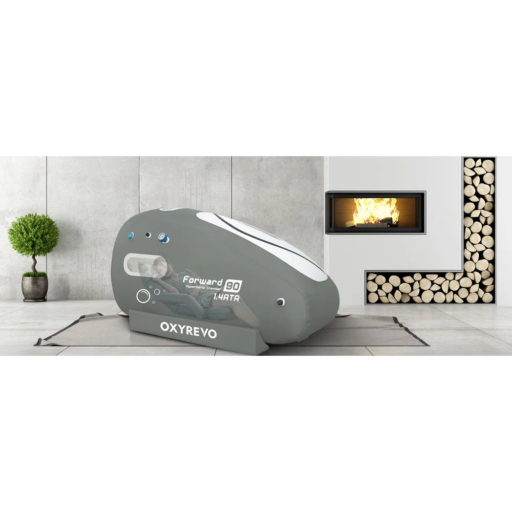 Wide banner of the 1.4 ATA Oxyrevo Forward90 Oxygen Chamber set up on a mat beside a lit fireplace