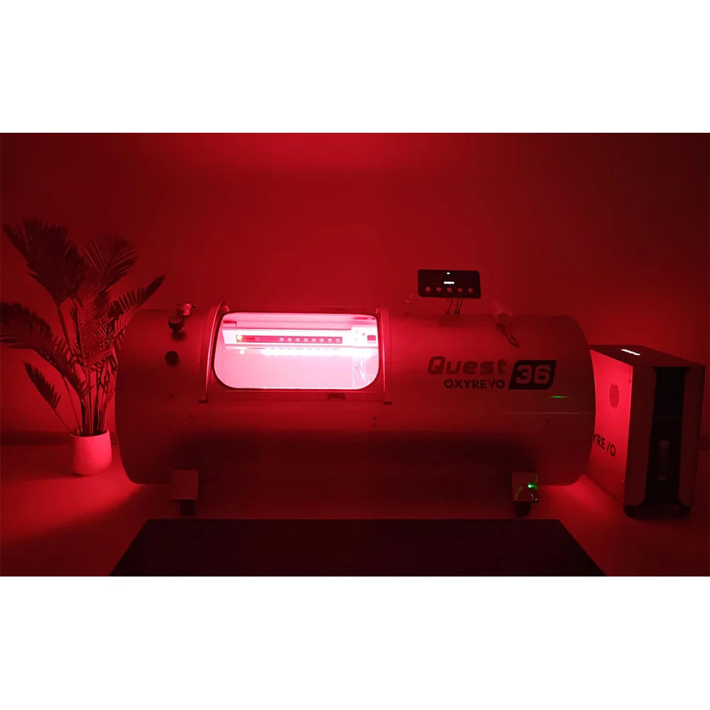 White OxyRevo Quest36 Hyperbaric Oxygen Chamber casting red light in a dark room during a combined session
