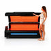 Woman in white activewear beside the open Apex M6 Full-Body Light Bed with both dense LED arrays glowing