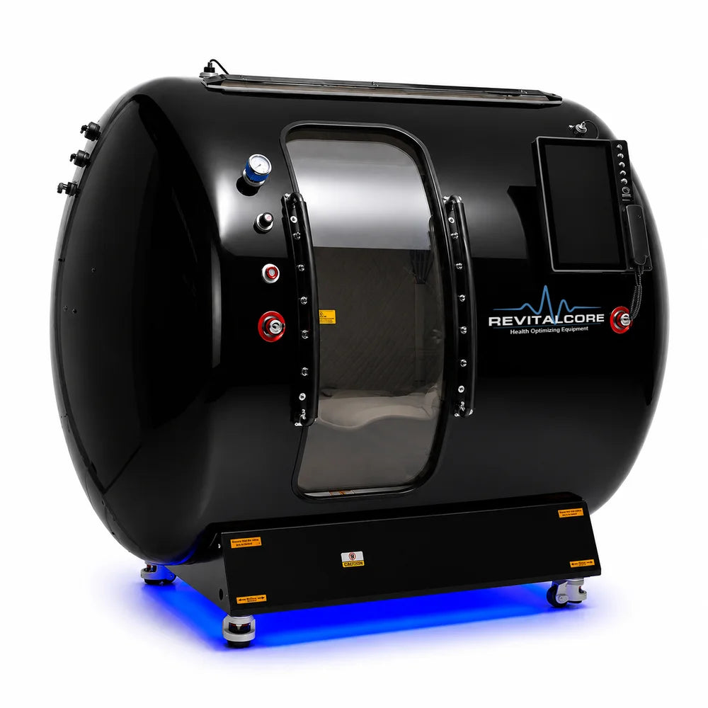 Angled studio shot of the RevitalCore Summit Duo Hyperbaric Chamber showing the curved stainless shell, bolted door and side hinges