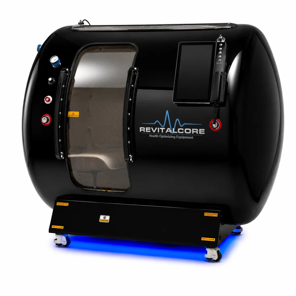 Three-quarter view of the RevitalCore Summit Duo Multiplace Hyperbaric Chamber with a cream chair visible through the tinted door window