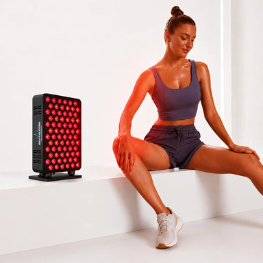 Woman stretching on a white ledge beside the glowing RevitalCore X-Aura Pro Therapy Device during a red light session