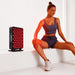 Woman stretching on a white ledge beside the glowing RevitalCore X-Aura Pro Therapy Device during a red light session