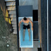 Aerial view down onto a man standing in the filled Revive Acrylic Plunge Tub beside outdoor stairs
