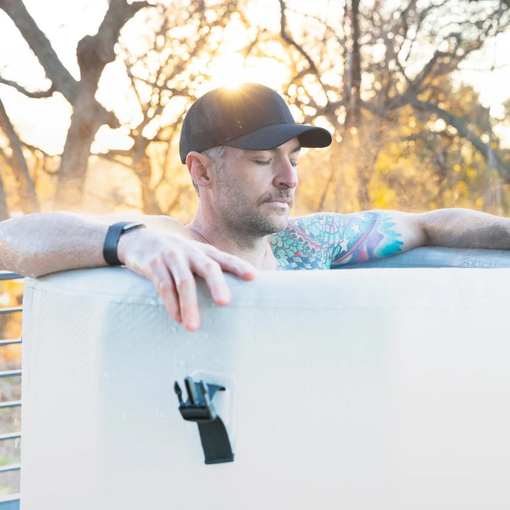 Man leaning on the padded rim at sunset while soaking in the Revive Plunge Inflatable Barrel Plunge Cold Plunge