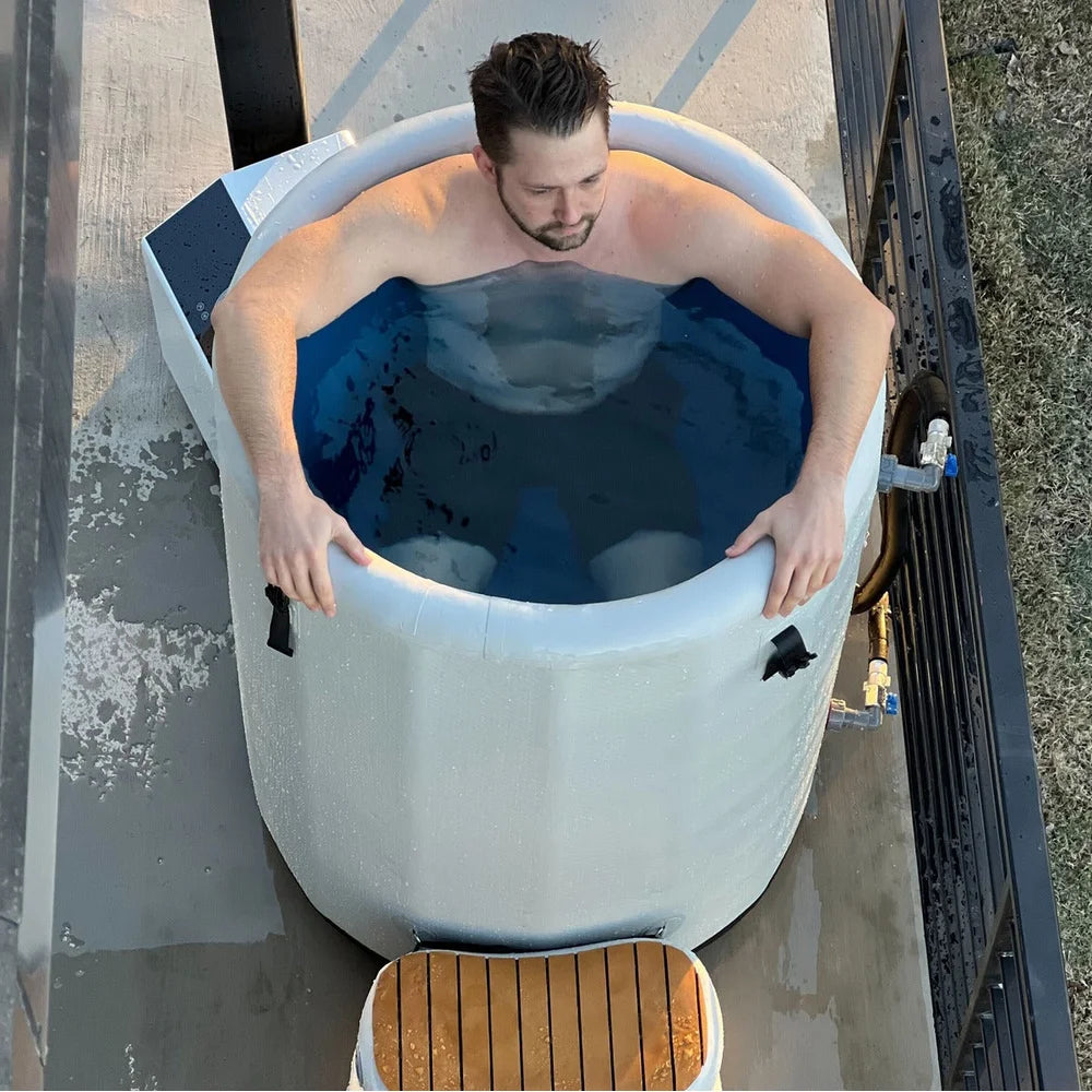 Aerial view of a man submerged inside the Revive Plunge Inflatable Barrel Plunge Tub with hose fittings alongside