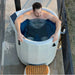 Aerial view of a man submerged inside the Revive Plunge Inflatable Barrel Plunge Tub with hose fittings alongside