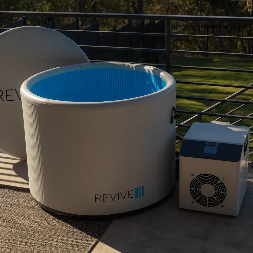 Water-filled Revive Inflatable Pod Plunge Ice Bath beside its chiller unit on a sunlit backyard deck