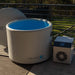 Water-filled Revive Inflatable Pod Plunge Ice Bath beside its chiller unit on a sunlit backyard deck