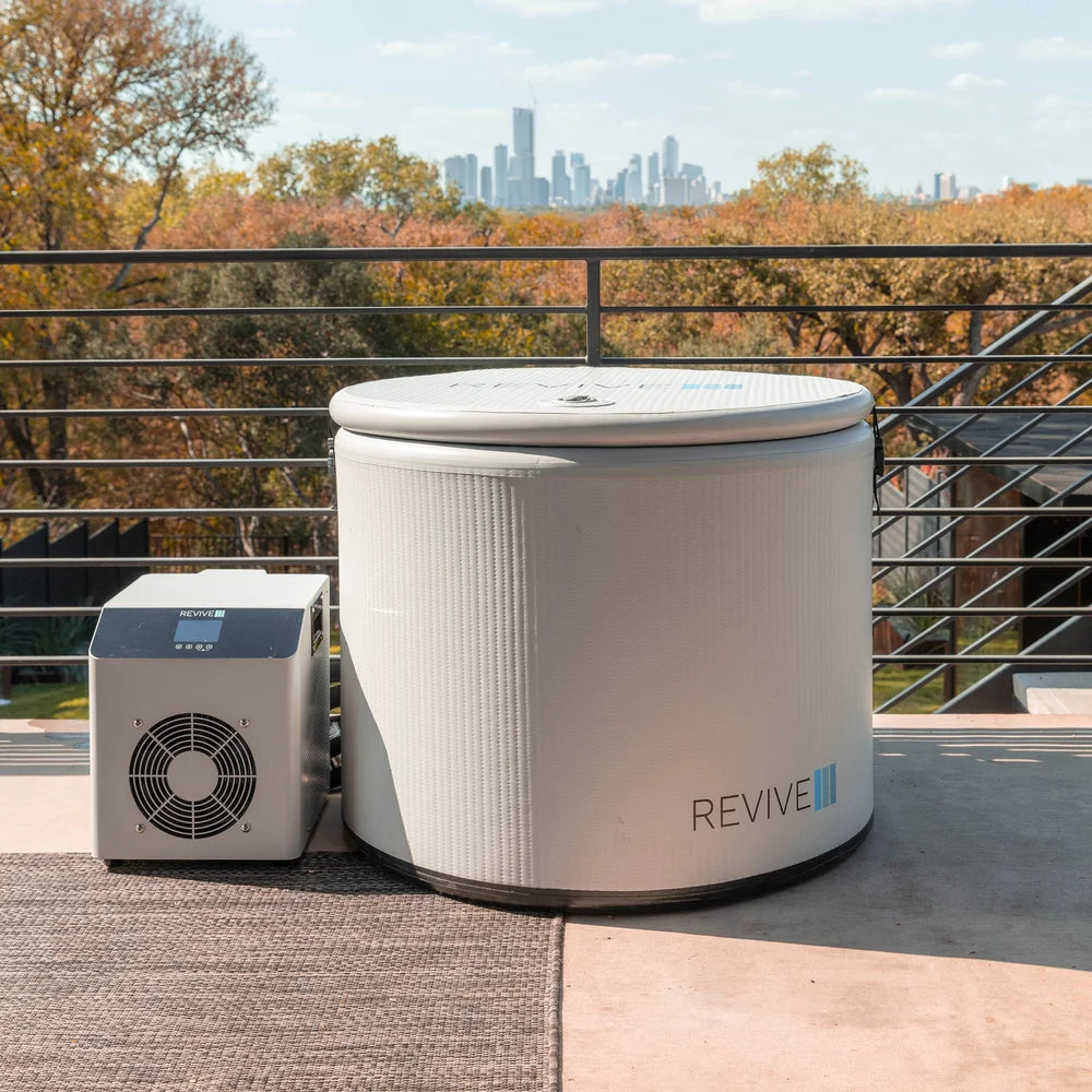 Lidded Revive Inflatable Pod Plunge Cold Plunge Pool and chiller on a rooftop deck framed by autumn trees