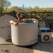Man relaxing inside the Revive Inflatable Pod Plunge Cold Plunge on a rooftop deck with a city skyline behind