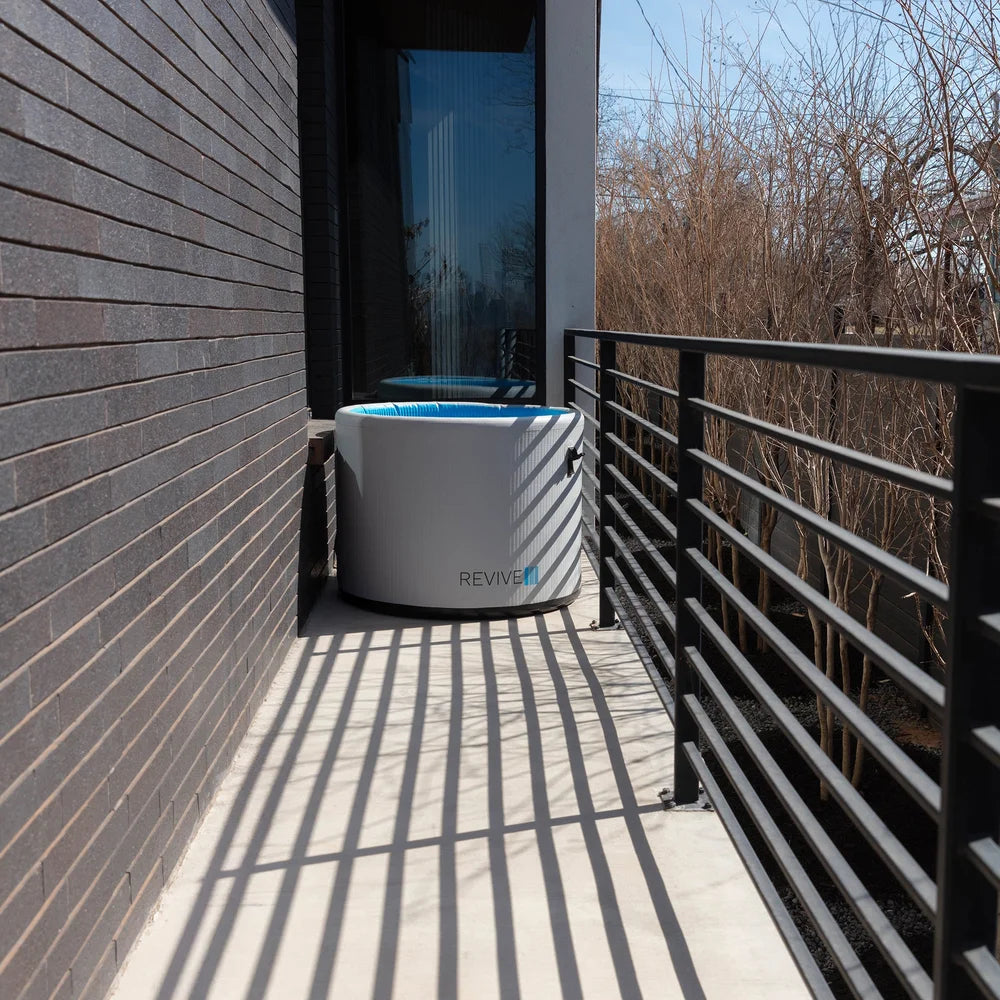 Revive Inflatable Pod Plunge Ice Bath Tub filled with water in a narrow passage between a brick wall and railing