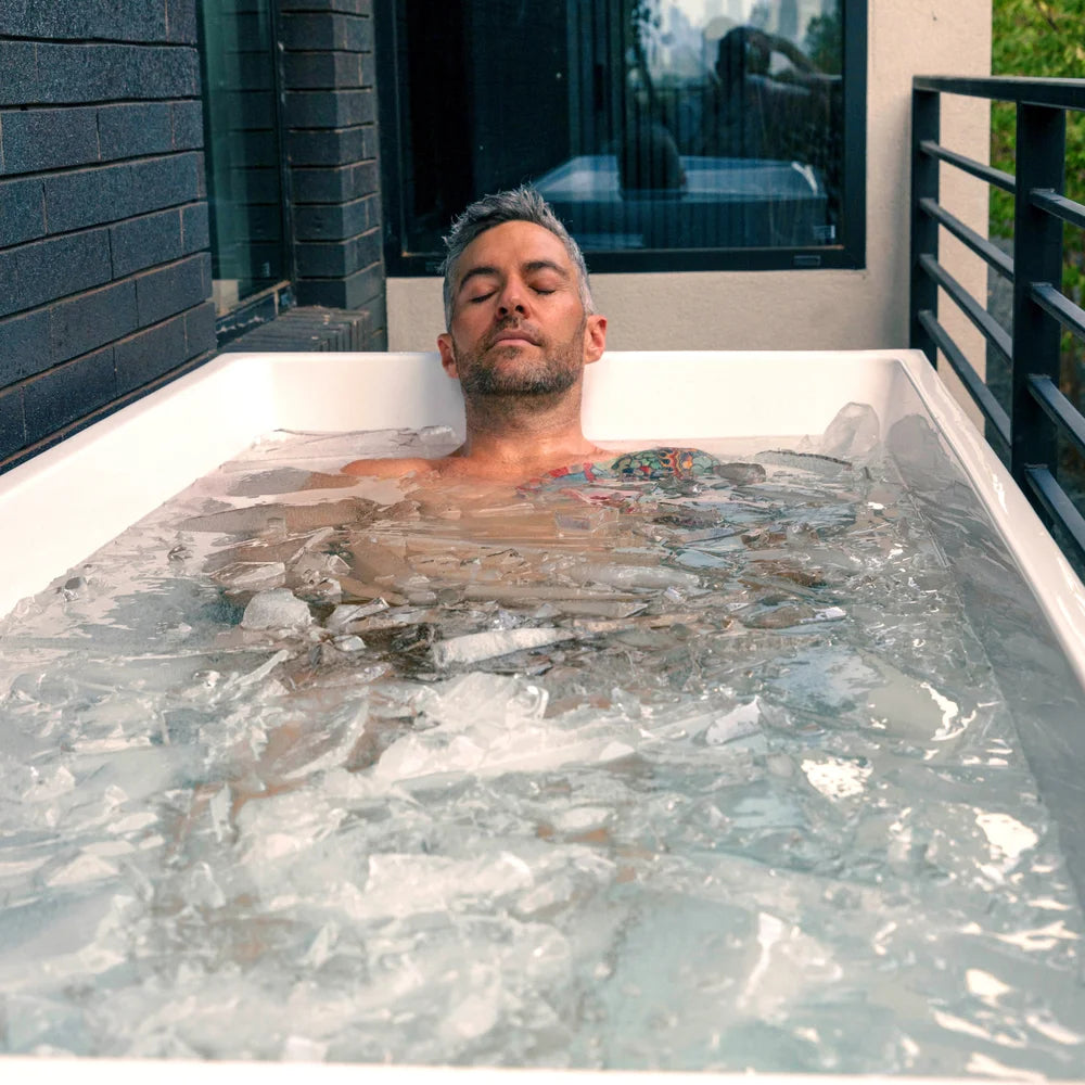 Man relaxing neck-deep in thick ice sheets inside the Revive Acrylic Plunge Tub on a balcony