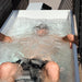 Person submerged in icy water during an overhead ice bath session in the Revive Acrylic Plunge on a patio