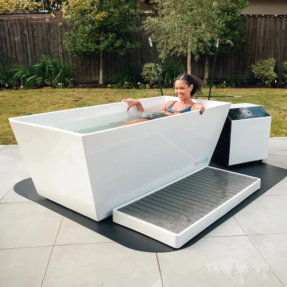 Woman smiling while seated in the Revive Acrylic Plunge Tub with step, mat and chiller in a backyard