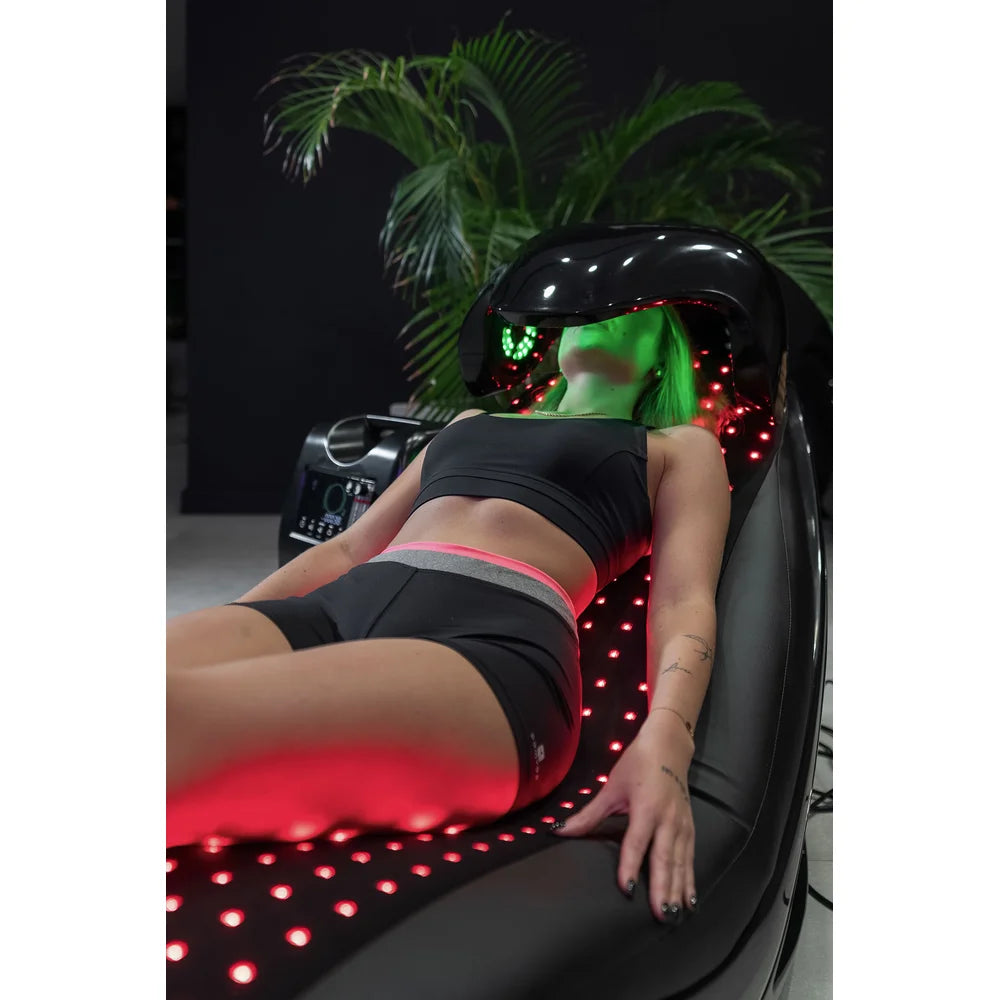 Woman resting along the red diode mattress of the Vacu Activ Red Couch Oxy with green dome light on her face
