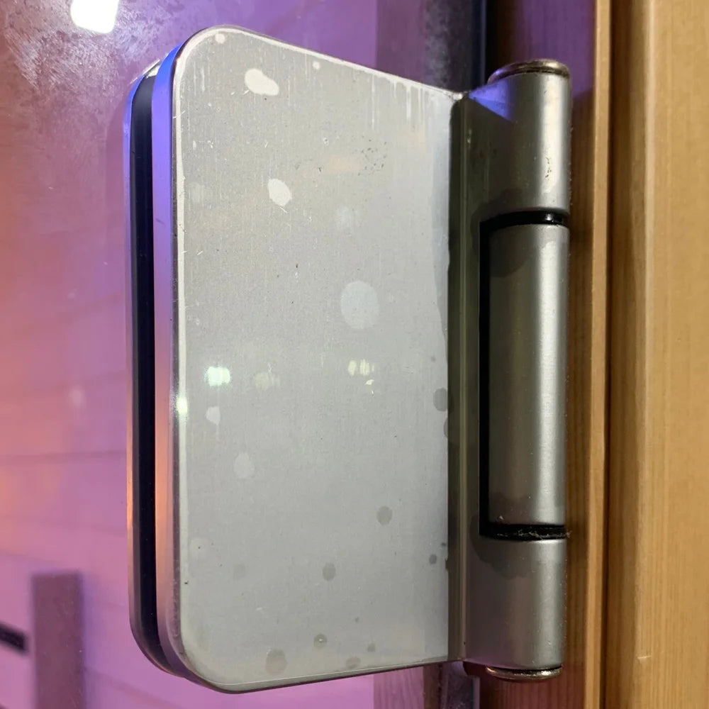 Metal hinge clamping the 6mm tempered glass door of the Blisspod Helsinki Chromotherapy Sauna frame
