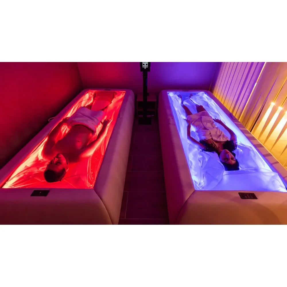 Two people relaxing side by side on a Tsb360 Dry Float Therapy Bed pair glowing red and blue in a dim spa room