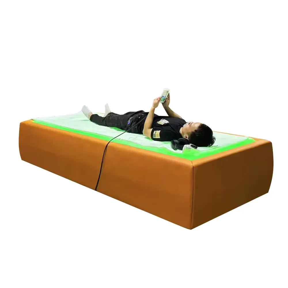 Man resting on a tan Tsb360 Dry Float Cryotherapy Bed with green illuminated membrane, phone in hand and headphones nearby
