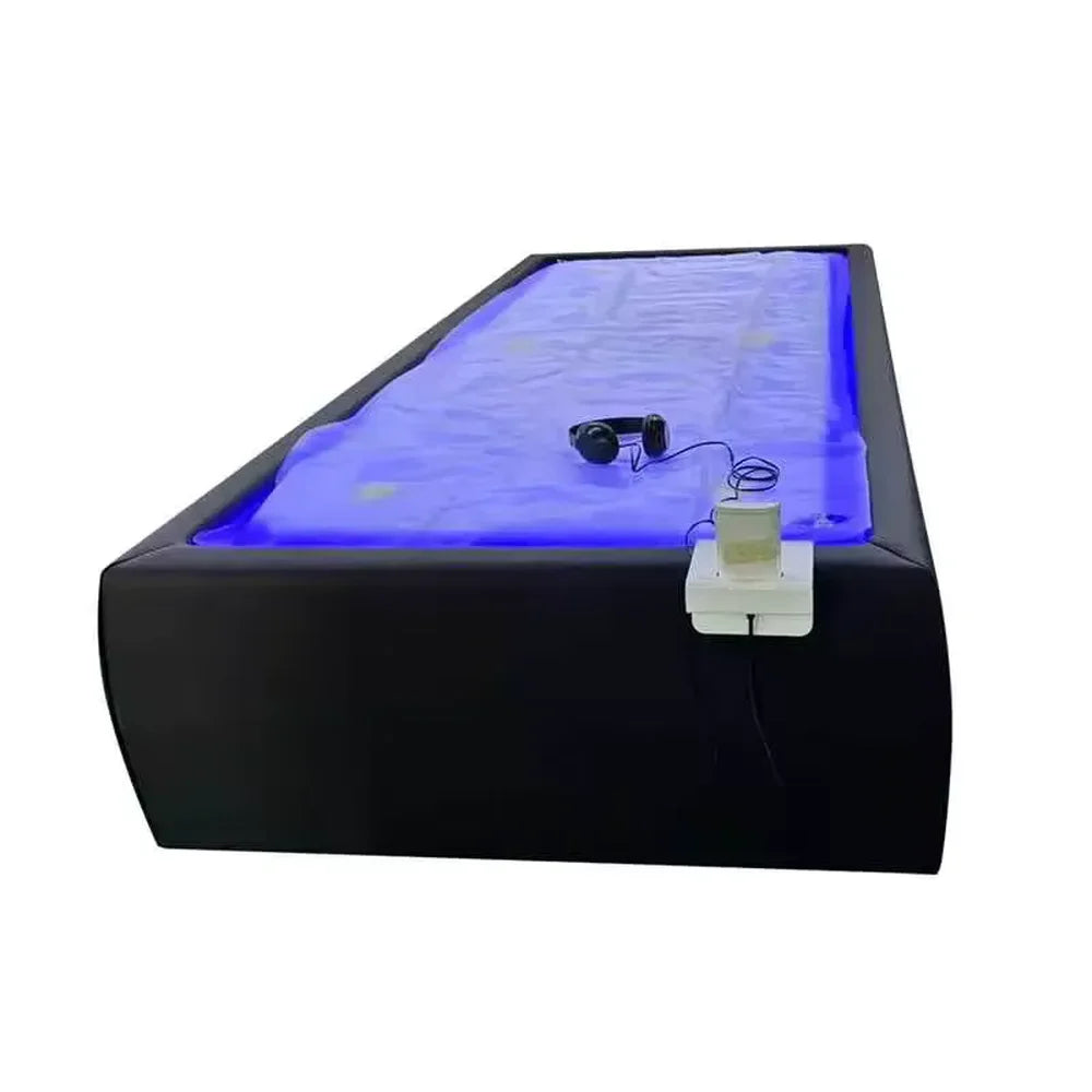 Black Tsb360 Dry Float Bed at an angle with blue-lit membrane, headphones and wired handheld controller on the side