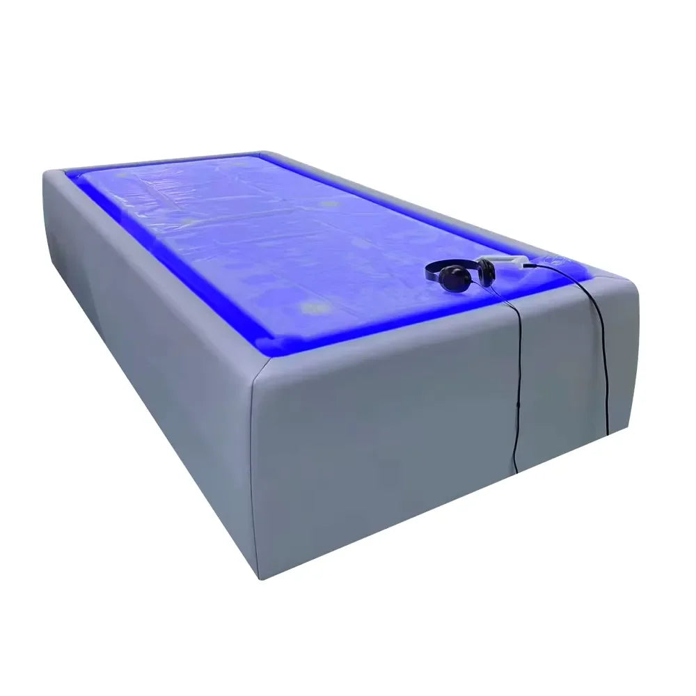 Grey Tsb360 Dry Float Recovery Bed seen from a front corner with blue glowing membrane and headphones on the surface