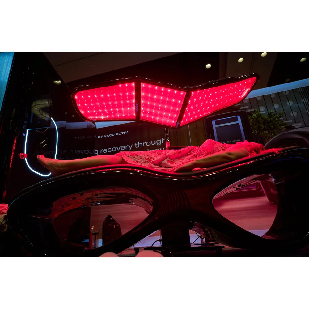 Client resting on the Longevity Longevity Bed during a session beneath the winged red LED canopy