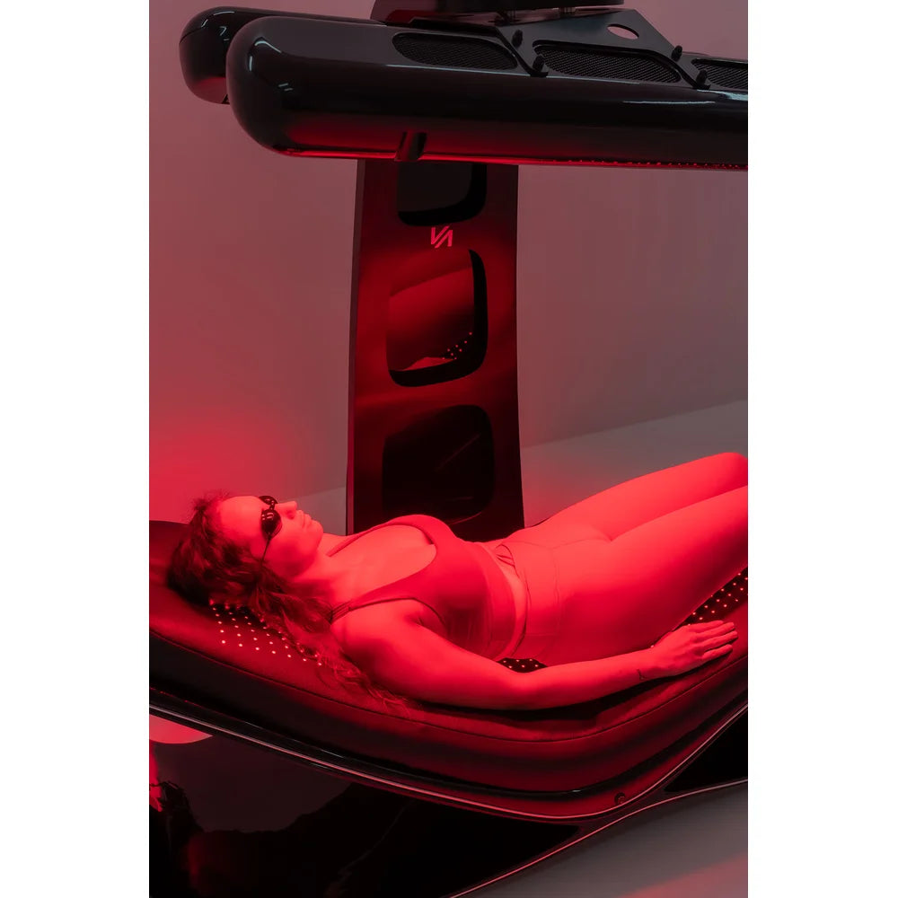 Goggled client bathed in red light on the Vacu Activ Red Couch 360 Red Light Therapy Couch mattress