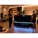 Clients in workout gear beside the Kore ELITE Full Body Light Therapy System in a warmly lit clinic lounge